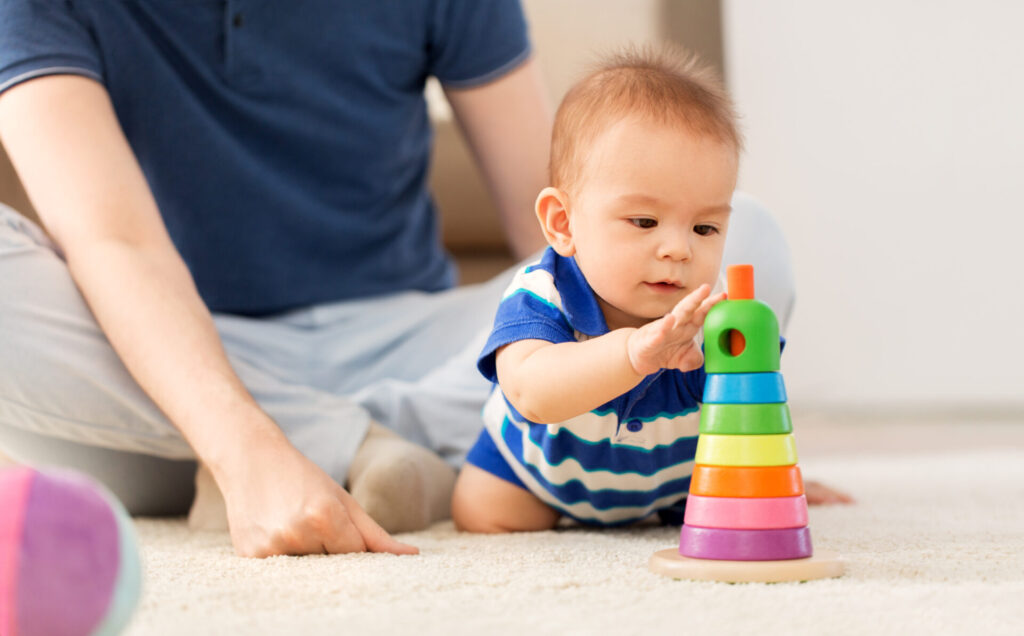 family, fatherhood and childhood concept - happy baby boy with father and toy pyramid at home