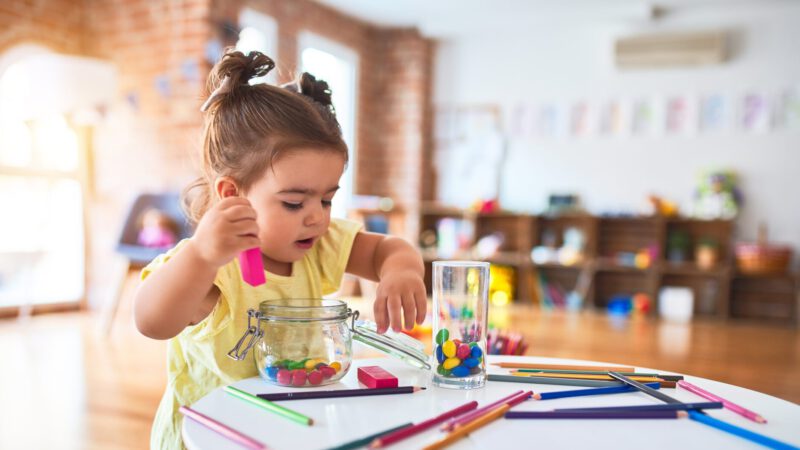 Beautiful toddler playing with wooden building blocks on the table at kindergarten