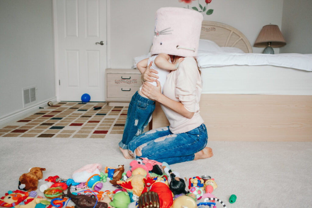 Mother parent playing with baby toddler in bedroom. Mom and kid boy girl with toy bin on heads. Family having fun at home. Candid authentic happy childhood lifestyle. Family life with kids.