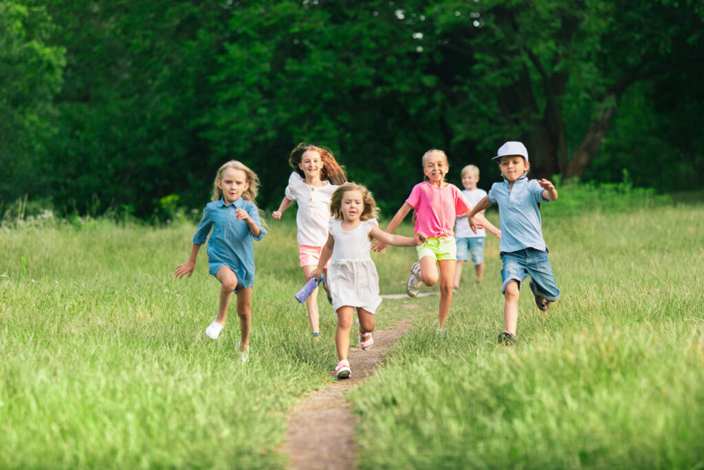 Kids, children running on meadow in summer's sunlight. Look happy, cheerful with sincere bright emotions. Cute caucasian boys and girls. Concept of childhood, happiness, movement, family and summer.